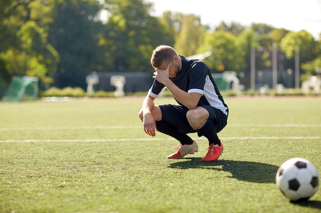 Sport, Fußball, Scheitern, Verlust und Menschen - trauriger Fußballspieler mit Ball auf dem Feld