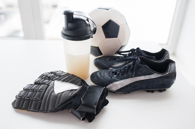 sport-, fußball- und sportgerätekonzept - nahaufnahme von fußball, stiefeln, torwarthandschuhen und proteinshake-flasche mit getränk