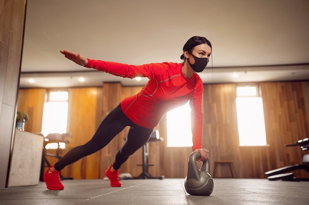 Sport Girl In Mask von Coronavirus macht Kettlebells Planking