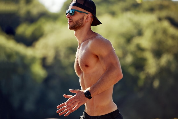 Sport in der Stadt Sportlicher Mann, der an einem schönen Sommertag im Stadtpark ohne Hemd für Fitness joggt