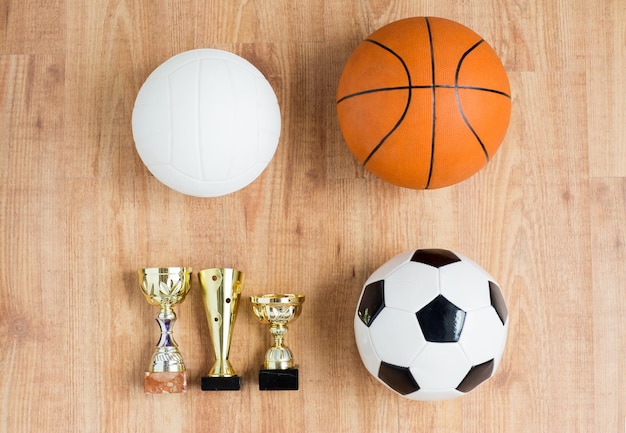 Sport-, Leistungs-, Meisterschafts-, Wettbewerbs- und Erfolgskonzept - Nahaufnahme verschiedener Bälle und goldener Tassen auf Holzhintergrund