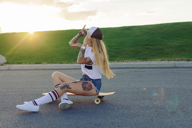 Sport-, Lifestyle-, Extreme- und People-Konzept - Schöne Mädchentattoos, die bei sonnigem Wetter Longboard auf der Straße in der Stadt reiten. Porträt-Hipster-Mädchen, das bei Sonnenuntergang mit einem Longboard lächelt.