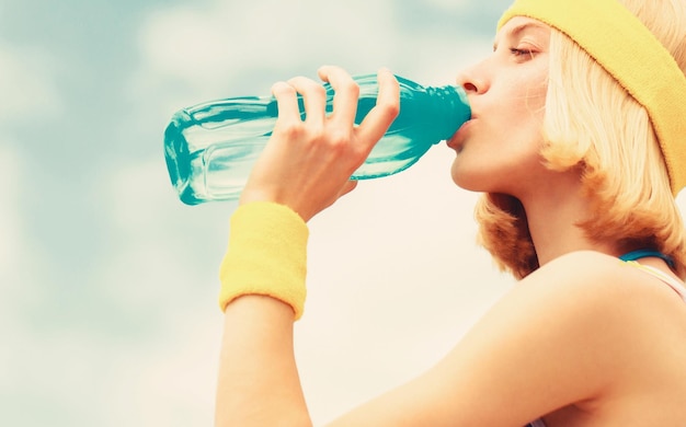 Sport-Mädchen trinkt Wasser aus einer Flasche auf Himmelshintergrund Gesunder Lebensstil-Konzept Trinken während des Sports Junge Frau Trinkwasser nach dem Lauf