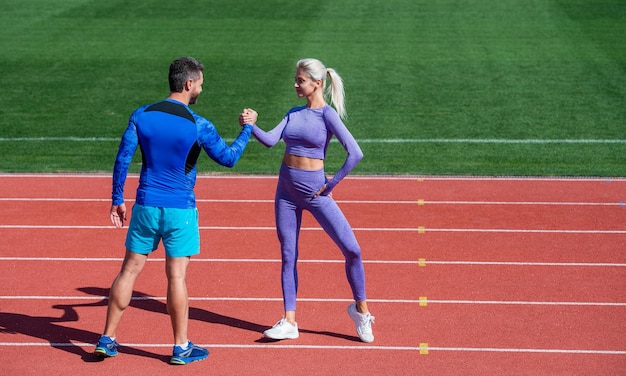 Sport-Mann- und -Frauen-Fitnesspartner feiern den Teamsieg mit Handschlag nach dem Training oder treten im Armdrücken auf der Stadion-Laufbahn-Arena im Freien an, Sporterfolg.\