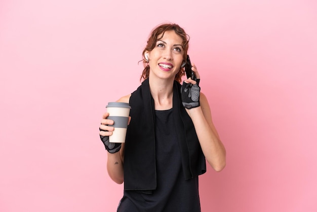 Sport Sport Frau mit Handtuch isoliert auf rosa Hintergrund mit Kaffee zum Mitnehmen und ein Handy