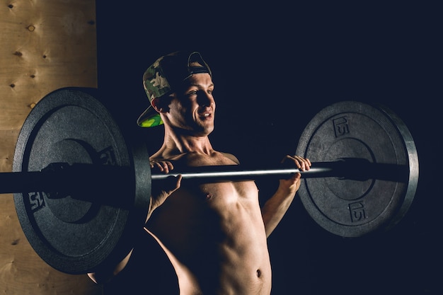 Sport, Training. Nahaufnahmeporträt eines muskulösen Manntrainings mit Langhantel im Fitnessstudio.