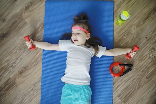 Sport und gesunder Lebensstil. Kind beim Sport zu Hause. Yogamatte Hantel und Springseil. Sporthintergrund mit Heimübungskonzept.