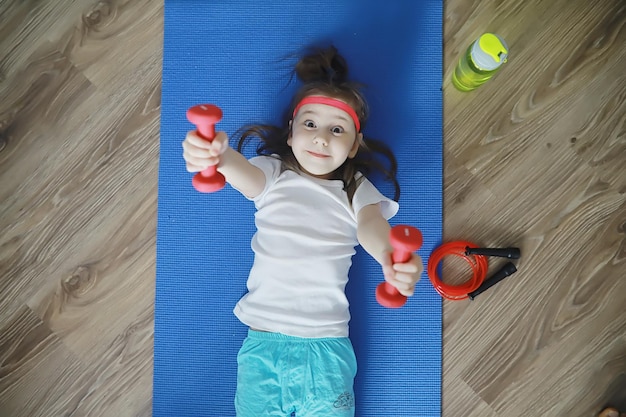 Sport und gesunder Lebensstil. Kind, das zu Hause Sport treibt. Yogamatte Hantel und Springseil. Sporthintergrund mit Heimübungskonzept.