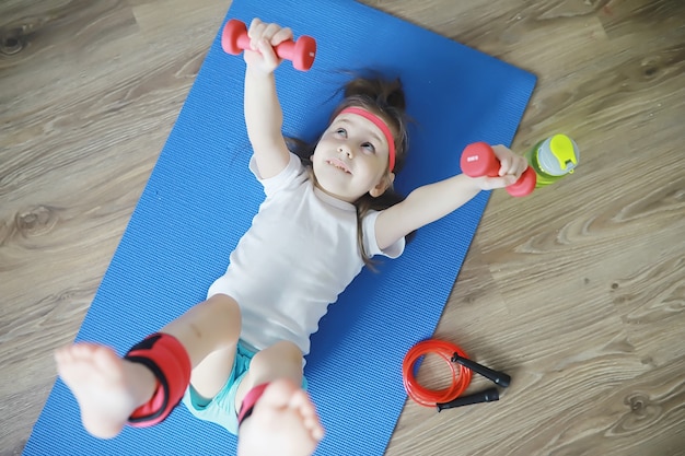 Sport und gesunder Lebensstil. Kind, das zu Hause Sport treibt. Yogamatte Hantel und Springseil. Sporthintergrund mit Heimübungskonzept.