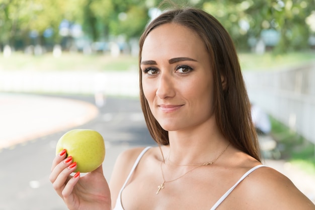 Sport und Gesundheit. Frau hält grünen Apfel. Sommeraktivität und Energie. Mädchen, das sonnig im Freien nährt. Obst und Vitamine.