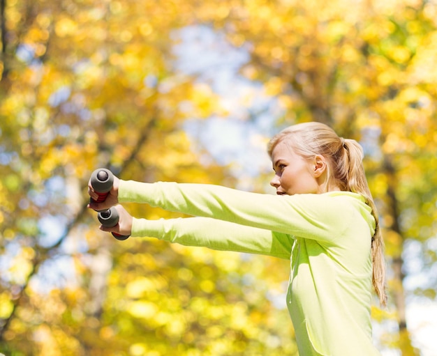 Foto sport- und lifestylekonzept - junge sportliche frau mit leichten hanteln im freien