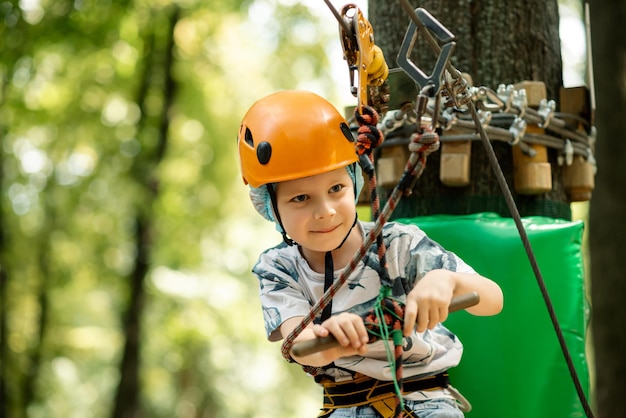 Sport Unterhaltung Erholung für ein Kind Ein kleiner Junge in einem Helm klettert im Seilpark