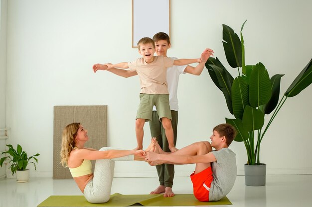 Sportfamilie eine Frau, ein Junge und zwei Teenager führen Gruppen-Yoga-Übungen mit Unterstützung durch, während sie sitzen