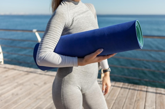 Sportfrau, die an einem sonnigen Tag eine Matte am Strand hält