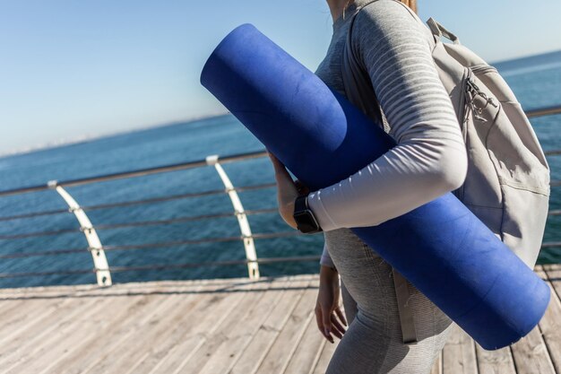 Sportfrau, die an einem sonnigen Tag eine Matte am Strand hält