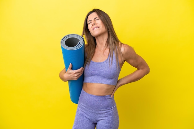 Sportfrau, die zu Yoga-Kursen geht, während sie eine Matte hält, die einen nicht gelben Hintergrund hat und unter Rückenschmerzen leidet, weil sie sich Mühe gegeben hat