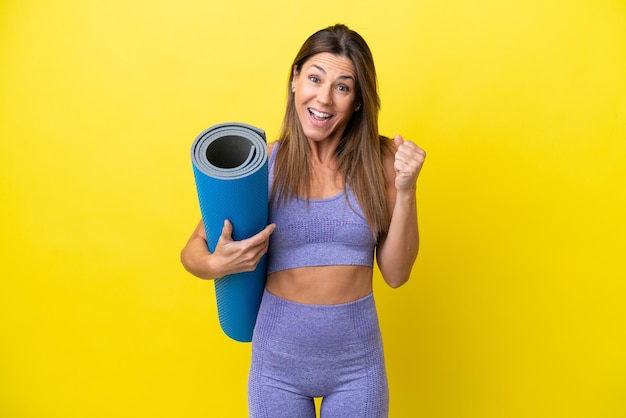 Sportfrau, die zu Yoga-Kursen geht, während sie eine Matte hält, die einen nicht gelben Hintergrund isoliert und einen Sieg in Siegerposition feiert