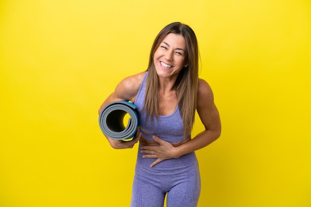 Sportfrau, die zu Yogakursen geht, während sie eine Matte hält, isoliert nicht gelben Hintergrund und lächelt viel