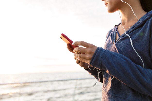 Sportfrau im Freien am Strand, die Musik mit Kopfhörern mit Handy hört.