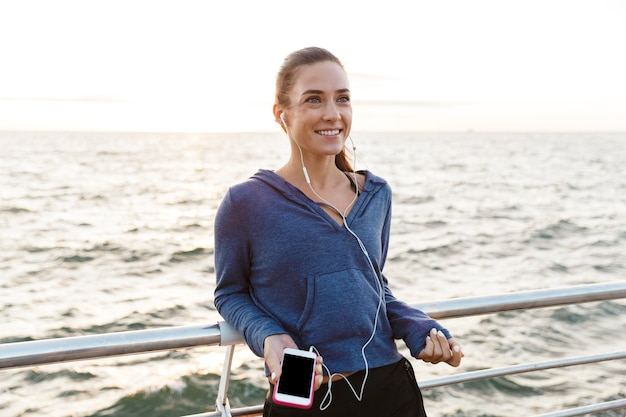 Sportfrau im Freien am Strand, die Musik mit Kopfhörern mit Handy hört.