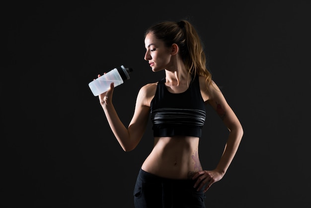 Sportfrau mit einer Flasche Wasser auf dunklem Hintergrund