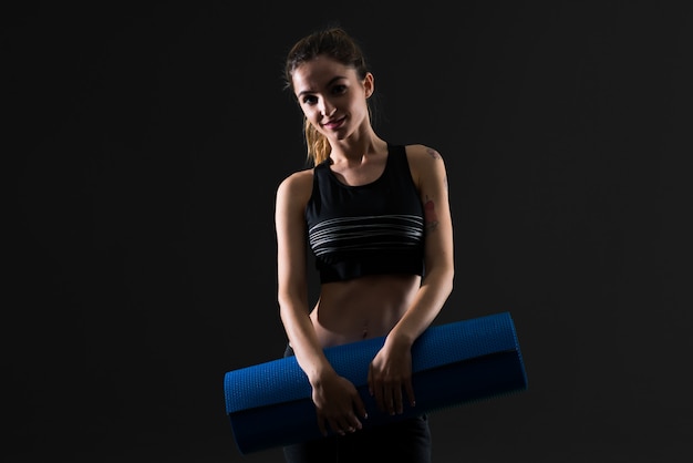 Sportfrau mit Matte auf dunklem Hintergrund