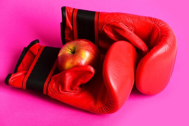 Sportgeräte und Obst isoliert auf rosa Hintergrund Paar Boxsportbekleidung aus Leder mit saftigem roten Apfel Boxhandschuhe in roter Farbe Trainings- und Fitnesskonzept