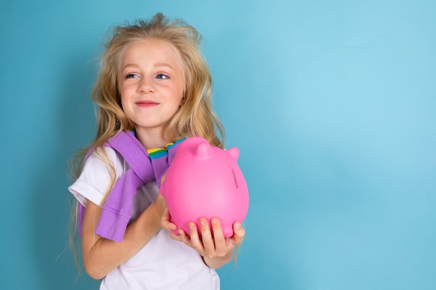 Sportjugendliches Mädchen im Sportanzug hält eine rosa Schweinespardose an der Wand