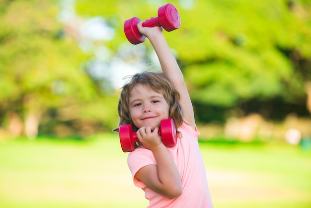 Sportkind mit Hantelkindersportjunge, der im Park aktiver gesunder Lebensstil trainiert