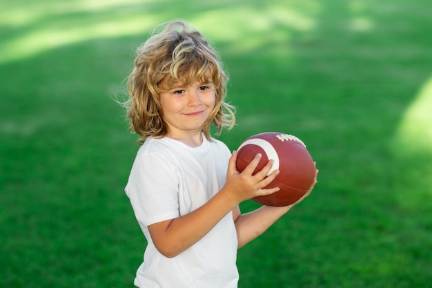 Sportkind Nettes Kind, das Spaß hat und American Football auf grünem Graspark spielt