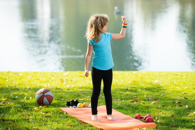 Sportkinder Kind mit starken Bizepsmuskeln Sportübung für Kinder Sportliche Kinder gesunder Lebensstil Kinderjunge, der draußen Hanteln hebt