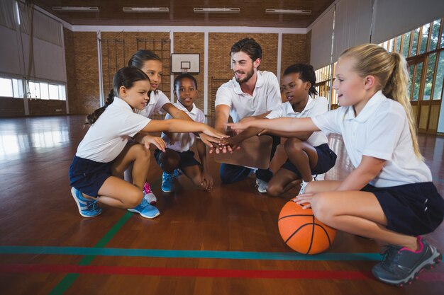 Sportlehrer und Schulkinder, die Handstapel im Basketballplatz bilden