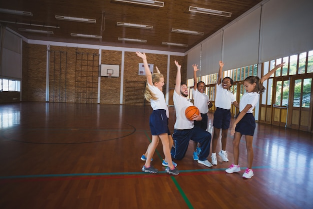 Sportlehrer und Schulkinder, die im Basketballplatz spielen