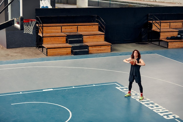 Sportler auf dem Basketballplatz. Ein Mann mit langen Haaren trainiert mit dem Ball auf dem Basketballplatz