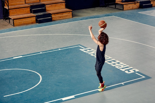Sportler auf dem Basketballplatz. Ein Mann mit langen Haaren trainiert mit dem Ball auf dem Basketballplatz