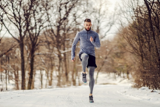 Sportler, der am verschneiten Wintertag im Wald läuft. Winterfitness, gesunder Lebensstil, kaltes Wetter