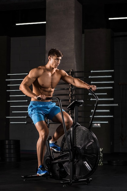 Sportler, der im Fitnessstudio Rad fährt, seine Beine trainiert, Kardio-Training fährt, Fahrrad fährt