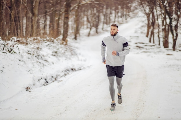 Sportler, der im Winter auf verschneiten Pfaden im Wald läuft. Wintersport, gesunde Gewohnheiten, Outdoor-Fitness