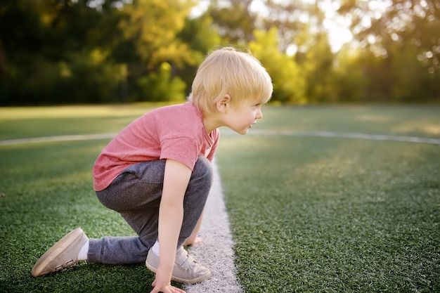 Sportler des kleinen Jungen, der fertig wird, im Schulstadion einen Abstand zu laufen.