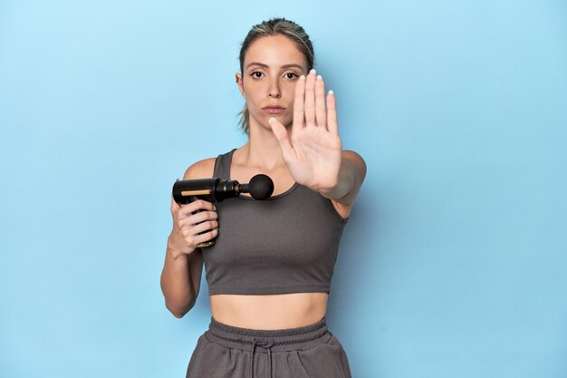 Sportler hält ein elektrisches Massagegerät und zeigt mit ausgestreckter Hand ein Stoppschild