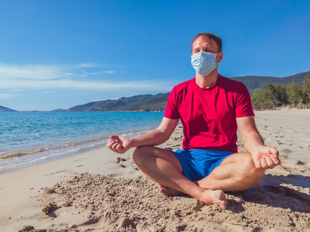 Sportler in medizinischer Maske trainiert während der Pandemie-Quarantäne im Park in der Nähe des Meeres im Freien Mentaler Schutz Atemenergie Übung Ausatmung Einatmung Konzentration Meditation Yoga-Pose