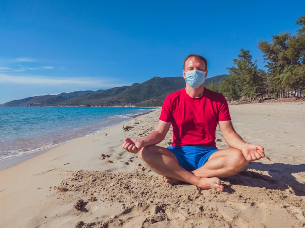 Sportler in medizinischer Maske trainiert während der Pandemie-Quarantäne im Park in der Nähe des Meeres im Freien Mentaler Schutz Atemenergie Übung Ausatmung Einatmung Konzentration Meditation Yoga-Pose