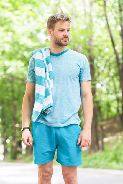 Sportler kurz nach dem Training. Mann mit Handtuch auf Naturlandschaft. Verschwitzt und müde. Sommer Strandzeit und Urlaub entspannen. Hygiene und Körperpflege. Sport und Wellness.