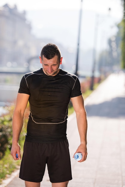 Sportler Läufer gießt Wasser aus der Flasche auf den Kopf, nachdem er an einem sonnigen Tag in der Stadt joggen gegangen ist