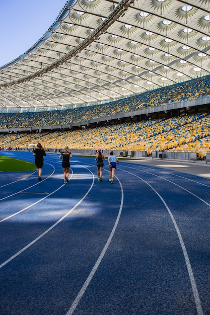 Sportler laufen auf der leeren blauen Laufstrecke im Olympiastadion vor dem Hintergrund leerer Tribünen