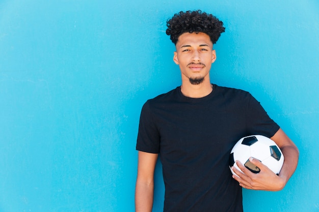 Foto sportler mit fußball unter arm nahe wand