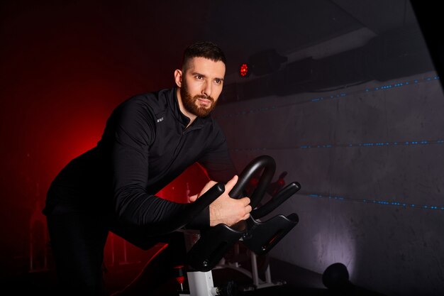 Sportler trainieren an Sportgeräten im Fitnessstudio, selbstbewusster und starker Mann im Trainingsanzug hat intensives Fahrradtraining im Fitnessclub,