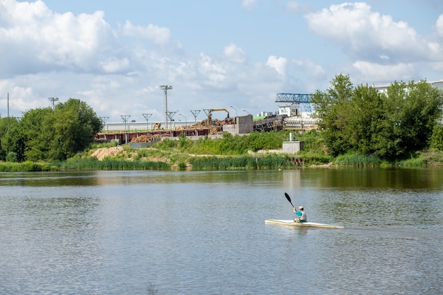 Sportler trainieren Kajakfahren auf dem Fluss vor dem Hintergrund eines Industrieunternehmens
