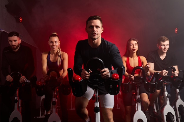 Sportler trainieren mit dem Fahrrad im Fitnessstudio, mit der Absicht der Gesundheitsfürsorge. kaukasische Männer und Frauen, die ycling, um Körper mit angespannten Muskeln gesund zu machen und das Gewicht zu reduzieren. männlich in der Mitte