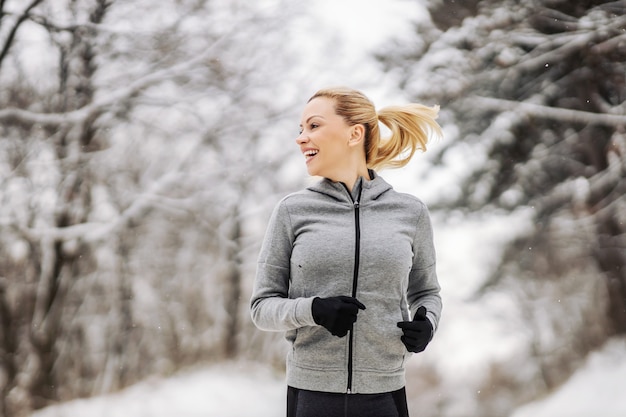 Sportlerin, die am verschneiten Wintertag im Wald läuft. Fitness in der Natur, Outdoor-Fitness, gesundes Leben